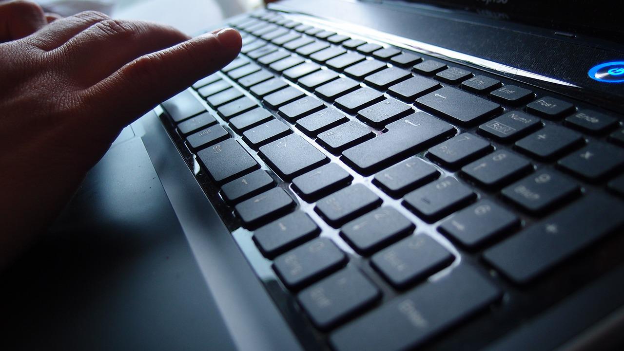 a hand hovers over a black keyboard with chicklet low-lift style keys, a brightly lit blue power button is visible in the upper corner